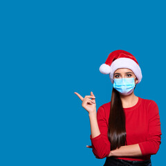 Fototapeta na wymiar Young Santa woman in Christmas hat face mask pointing index finger on product on blue isolated background.
