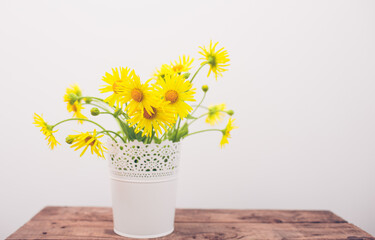 yellow flowers in a vase on a wooden background