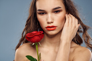 Woman portrait with red rose near the face on gray background and makeup curly hair