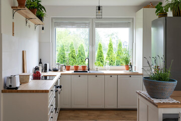 Kitchen with big window, minimal design, simple decor, white furniture and wooden kitchen counter. 