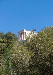 distant view of Athena Nike ancient temple between trees and clear blue sky, Athens Greece