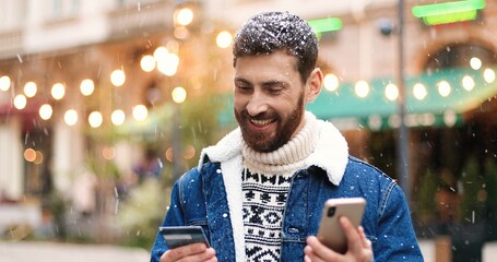 Close up portrait of joyful Caucasian guy shopping online on smartphone and paying with credit...