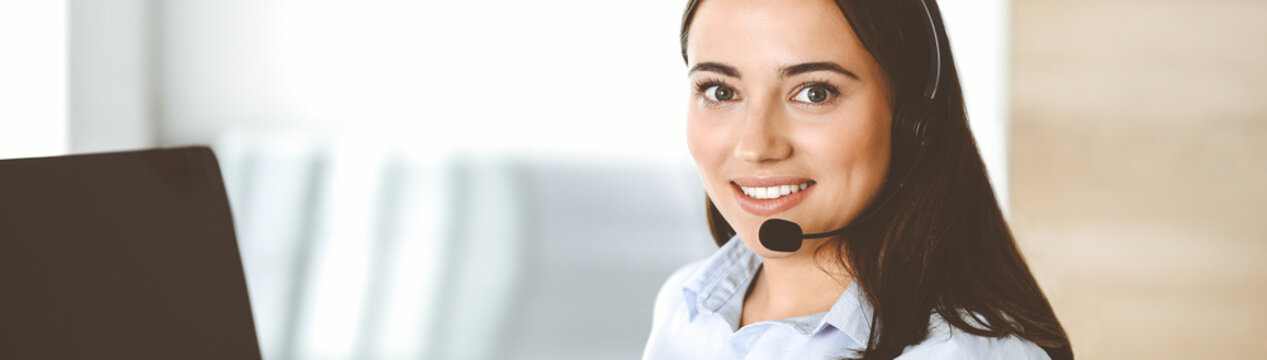 Brunette female customer service representative in a headset is consulting clients online. Call center and business people concept