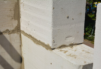 A close-up of a corner of a masonry wall made from autoclaved aerated concrete blocks (AAC) with a sawn concrete brick for a window area.