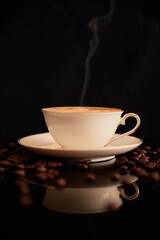 Closeup of a steaming hot cup of coffee on a black surface. Cup of cappuccino and coffee beans on a black surface.