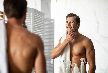 Confident young guy looking in the mirror, touching chin