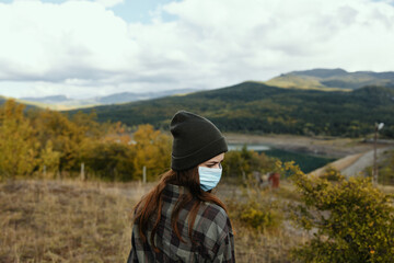 A woman in a warm hat with a medical mask on her face in the forest in nature