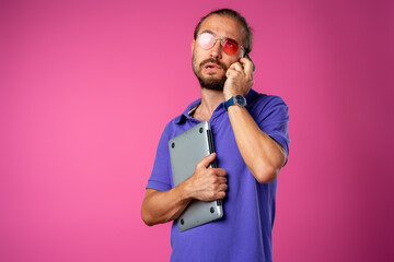 Man in glasses standing with laptop against pink background