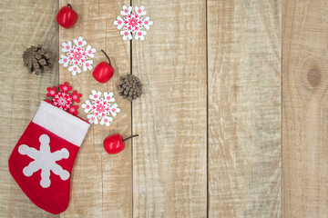 Festive composition of Christmas Santa sock filled with gifts: red and white snowflakes, fir cones and red small toys on wooden background. Christmas or New Year greeting card with copy space.