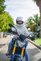 Woman happy with her motorcycle, equipped with helmet and white jacket