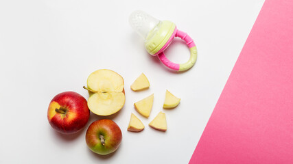 first feeding.Baby nibbler with food on white and pink background. whole and cut apple. Flat lay