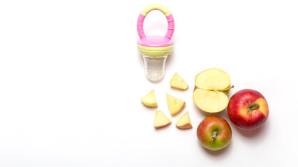 first feeding. Baby nibbler with food on white and pink background. whole and cut apple. Flat lay