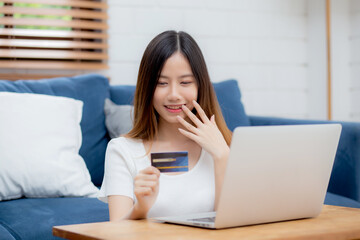 Young asian woman sit on sofa using laptop computer shopping online with credit card buy to internet and surprise, happy girl payment with e-business on couch, success and excited, business concept.