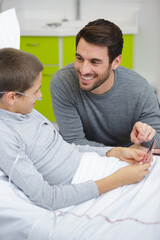 child lying on a medical bed next to his dad
