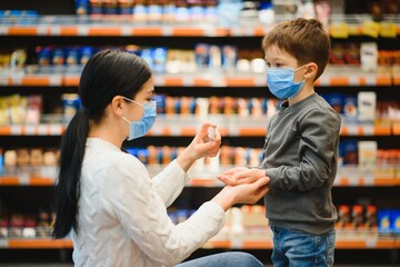 Mother applies sanitizer for cleaning son's hands in public crowded place. Shopping mall.
