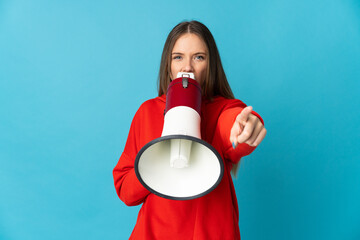 Young Lithuanian woman isolated on blue background shouting through a megaphone to announce something while pointing to the front