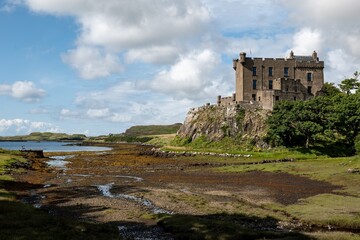 Fototapeta premium Dunvegan Castle on a top a hill at Isle of Skye, Scotland during the low tide with blue sky