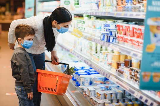 Shopping With Kid During Virus Outbreak. Mother And Child Wearing Surgical Face Mask Buying Fruit In Supermarket. Mom And Little Boy Buy Fresh Vegetable In Grocery Store. Family In Shop.