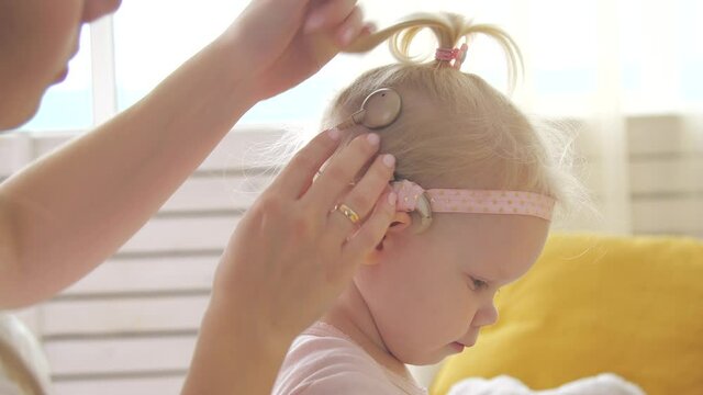 Concept of hearing impairment and their treatment. Mom connects a cochlear implant for her daughter