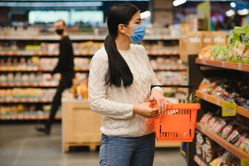 Alarmed female wears medical mask against coronavirus while grocery shopping in supermarket or store- health, safety and pandemic concept - young woman wearing protective mask and stockpiling food