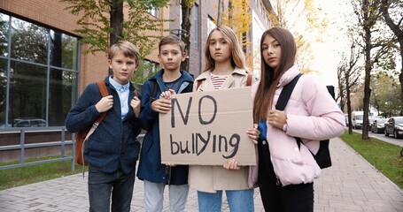 Portrait of cute serious teen schoolkids standing outdoors near school with 