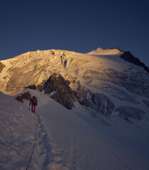 mountaineer on a rope going toward the distant peak while the sun is rising