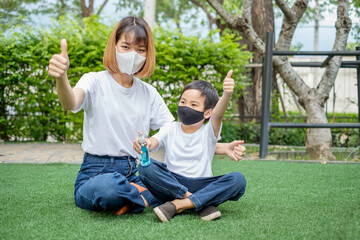 Asian mother and son thumb up and hold alcohol spray bottle sitting home garden