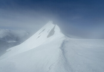 Fototapeta na wymiar snowy high mountain peak shrouded in mist at sunrise