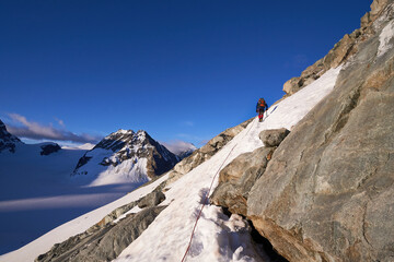 mountaineer thethered to a rope climbing up a snowy mounatin side in summer with Petit Mont Colon...