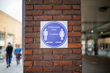 Sign on brick wall requesting people to keep a safe distance