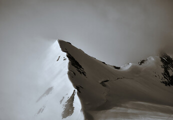 beautiful curved mountain peak and ridge peeking out of the clouds in black and white