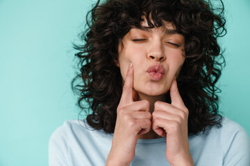 amusing beautiful curly girl grimacing and pointing fingers at her cheek