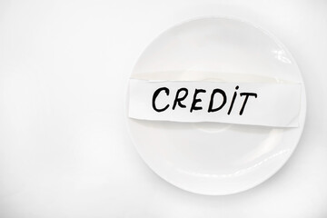 On a light background there is a white plate with a piece of paper with the inscription credit on it. The concept of poverty and business