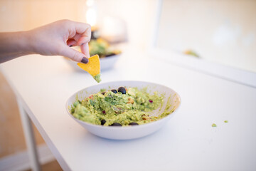 Female hand dipping nachos in guacamole sauce with olives