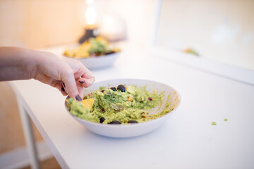 Female hand dipping nachos in guacamole sauce with olives