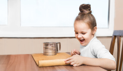 cute preschoolgirl girl is sitting at the table and is going to prepare the dough for modeling. cooking concept. on the kitchen