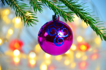 Purple Christmas decor ball on green tree branch of a Christmas tree on a background of Christmas lights new year background, no focus, blur, blurry