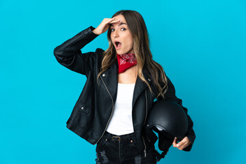 Romanian woman holding a motorcycle helmet isolated on blue background doing surprise gesture while looking to the side