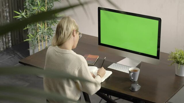 Distance learning course, woman doing remote telework concept working from home office.Green screen display. Female student, online teacher conference calling by web cam using computer taking notes.