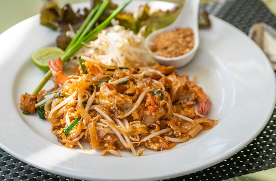 Pad Thai or Thai traditional stir-fried noodle with shrimps, close up juicy Pad Thai on white dish, beautiful food decoration, natural light image.