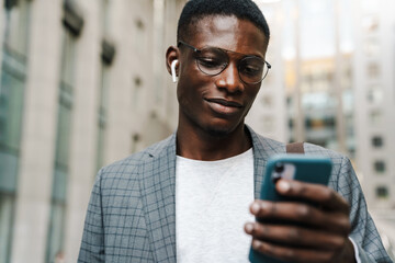 Pleased african american man in earphones using mobile phone