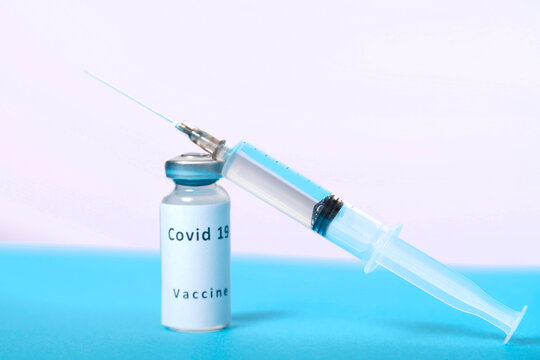 A syringe and a vial of coronavirus vaccine are on a blue table, top view.