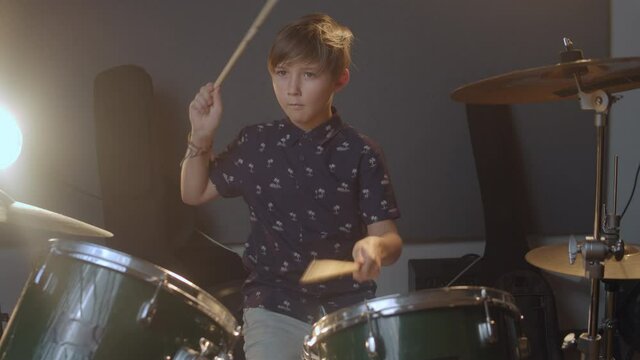 Creative kids. Young musician. Kid playing drums in the music produciton studio. A blonde hair young boy in a fancy shirt learning how to play songs.