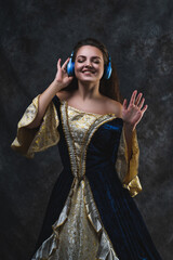 Happy beautiful woman in renaissance dress listens to music in wireless headphones on abstract dark background