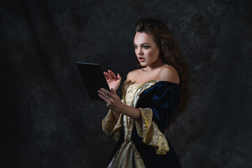 Beautiful woman in renaissance dress uses tablet on abstract dark background