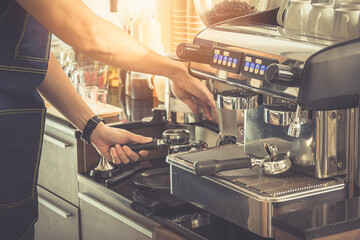 Close up, Barista making an espresso with a classic Italian coffee machine with steam and sunlight in background.