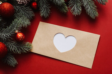 A closed envelope with a heart cut out on it next to Christmas branches and decorations, balls. Christmas winter holiday New Year composition