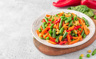 Various steamed vegetables close-up. Boiled peas, corn, string beans, carrots, and peppers in a...
