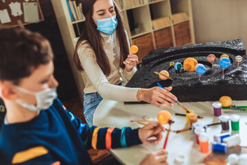 Happy school boy and girl with protective mask making a solar system for a school science project at home