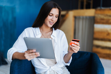 Beautiful millennial woman using bank card to pay for goods purchased online. Internet shopping